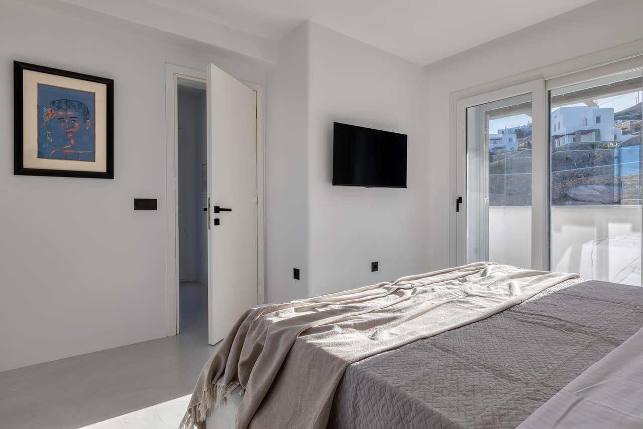 A bedroom in grey and linen, a sliding door onto the balcony and the hillside beyond