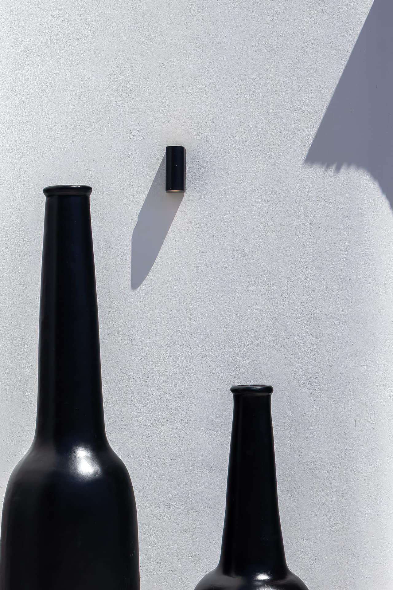 Two tall black bottles against a white plaster wall