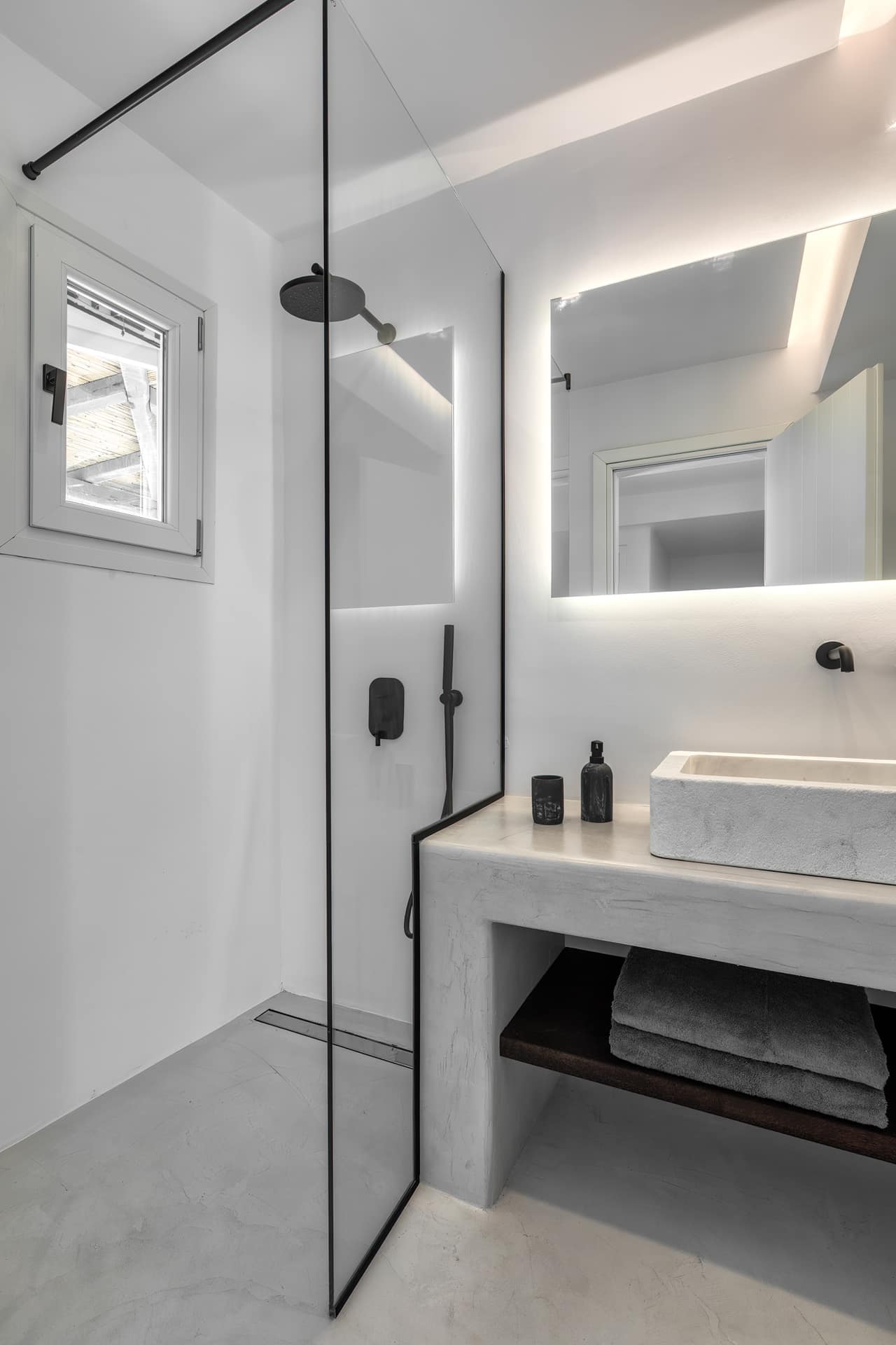 A walk-in rain shower behind a black-framed screen, a carved stone basin alongside