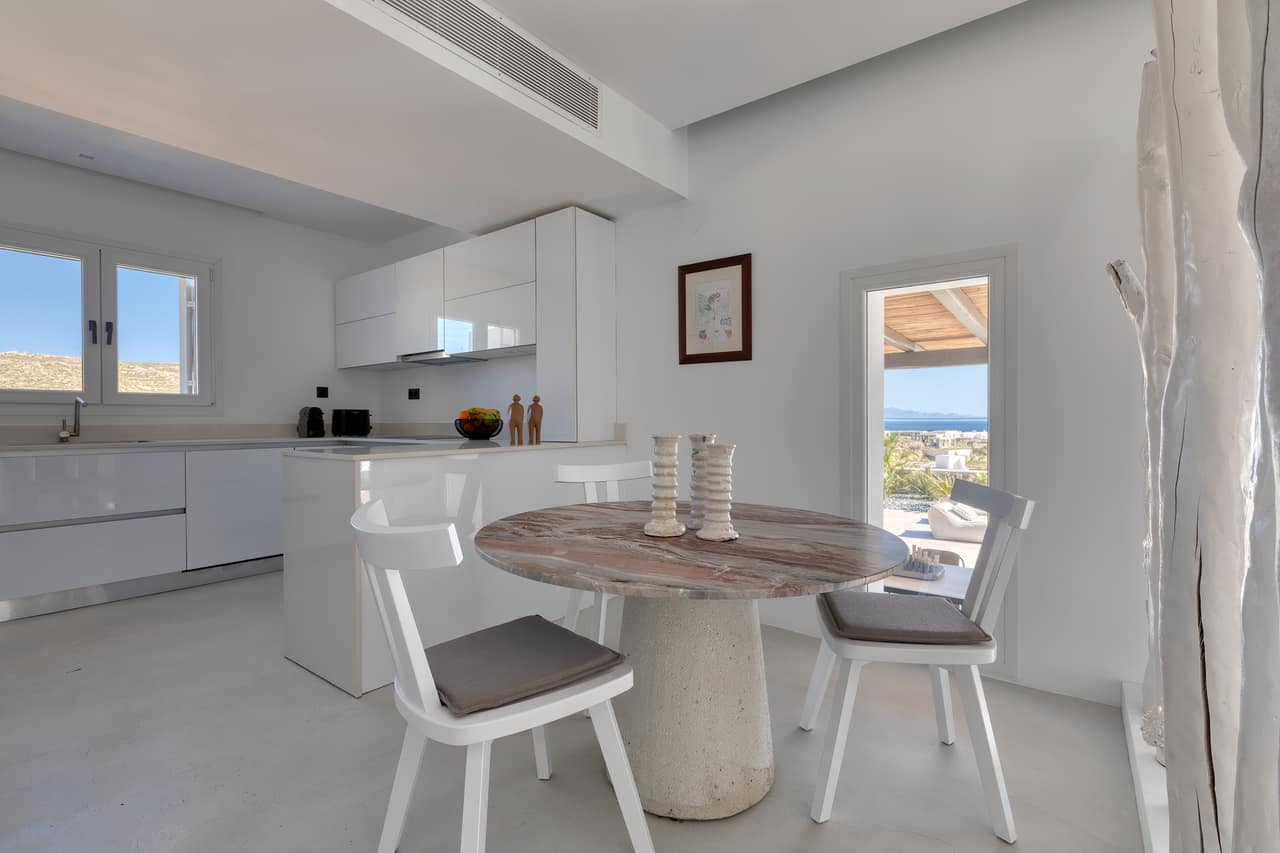 The white kitchen and a round marble table on a stone plinth, the sea through the open door
