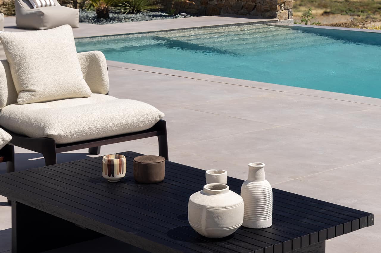 A bouclé chair and pale vases at the pool's edge
